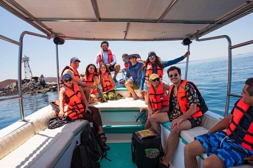 A group of people on a boat wearing life jackets, with a rocky shoreline in the background. 3
