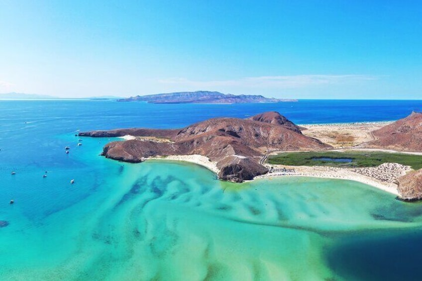 A coastal landscape with clear turquoise waters, rocky outcrops, and distant mountains. 1