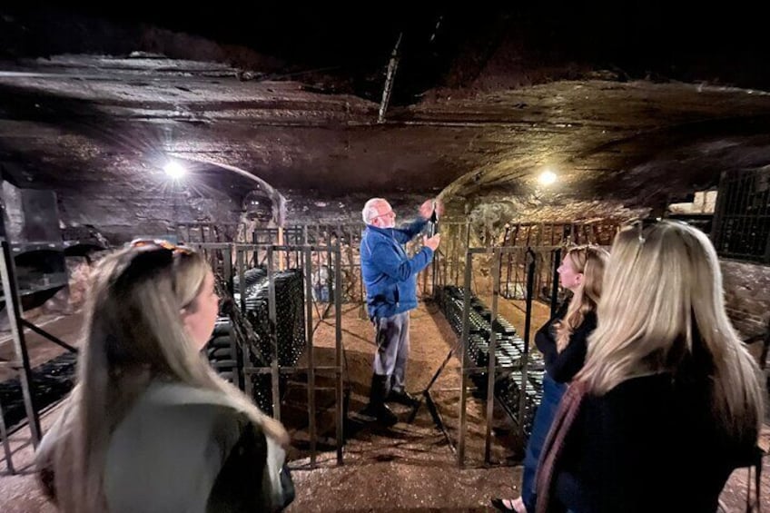 A group of people inside a cave with metal railings and a person in a blue jacket standing near the entrance. 1