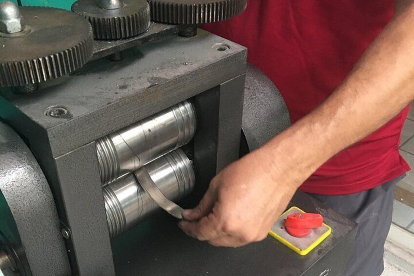 A person operating a machine with cylindrical rollers and a red button. 3