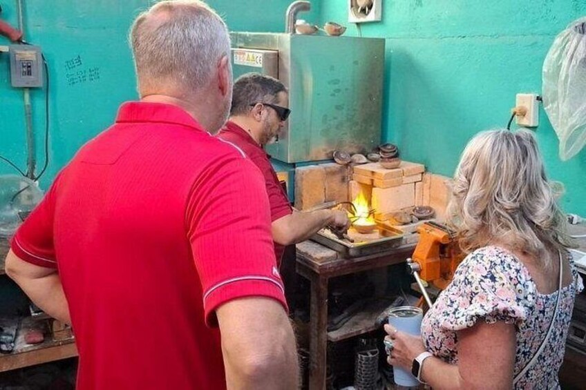 A person in a red shirt working with a fire, another person in a floral dress observing, and a third person holding a drink. 2
