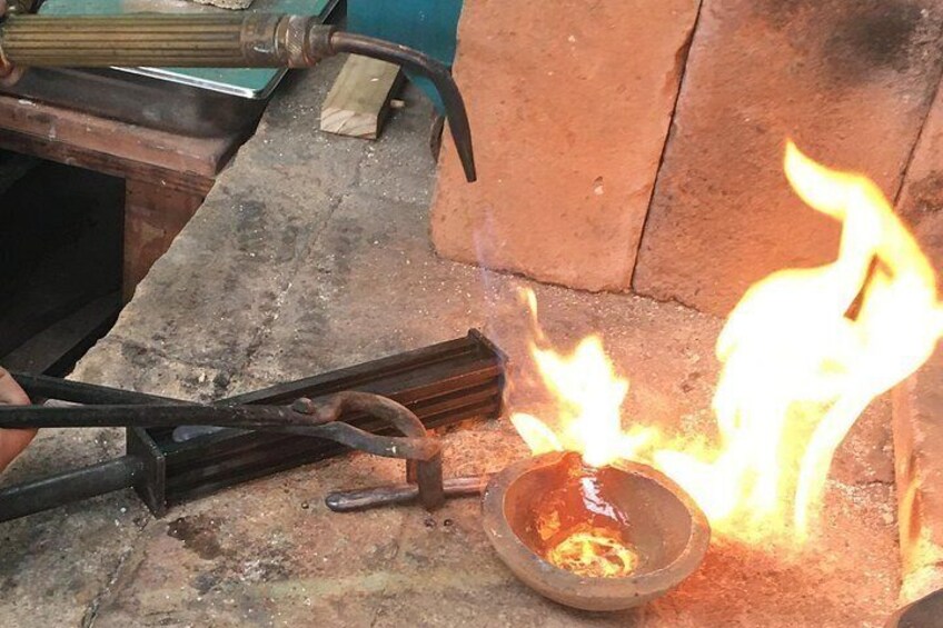 A metalworking process with flames, a metal rod, and a bowl on a workbench. 5