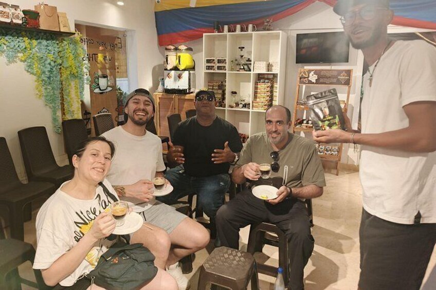 A group of people sitting and standing indoors, some holding plates with food. 1
