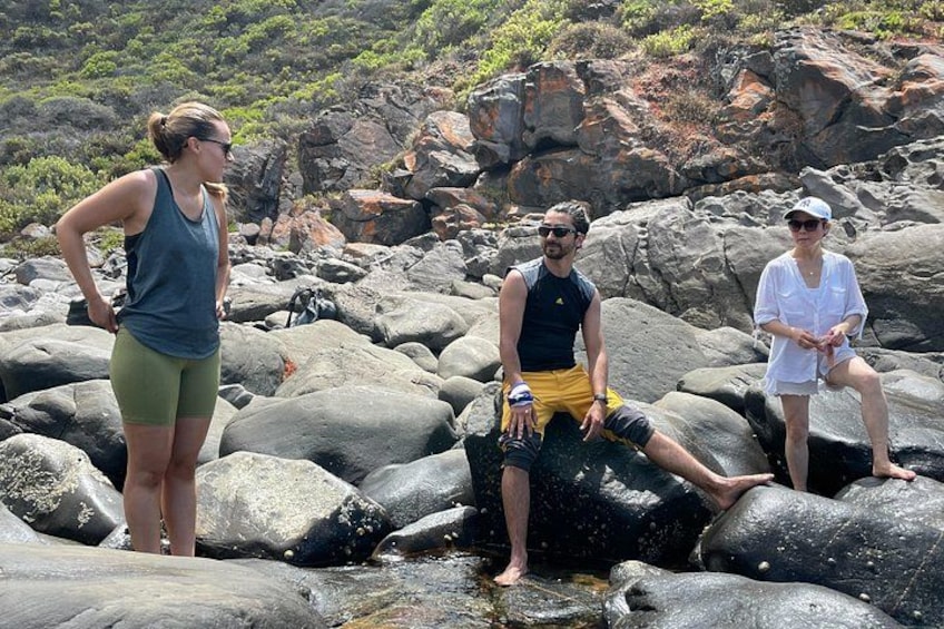 Three people on rocky terrain with greenery in the background. 5
