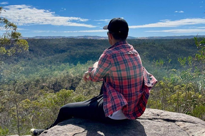 A person sitting on a rock overlooking a forested valley. 2