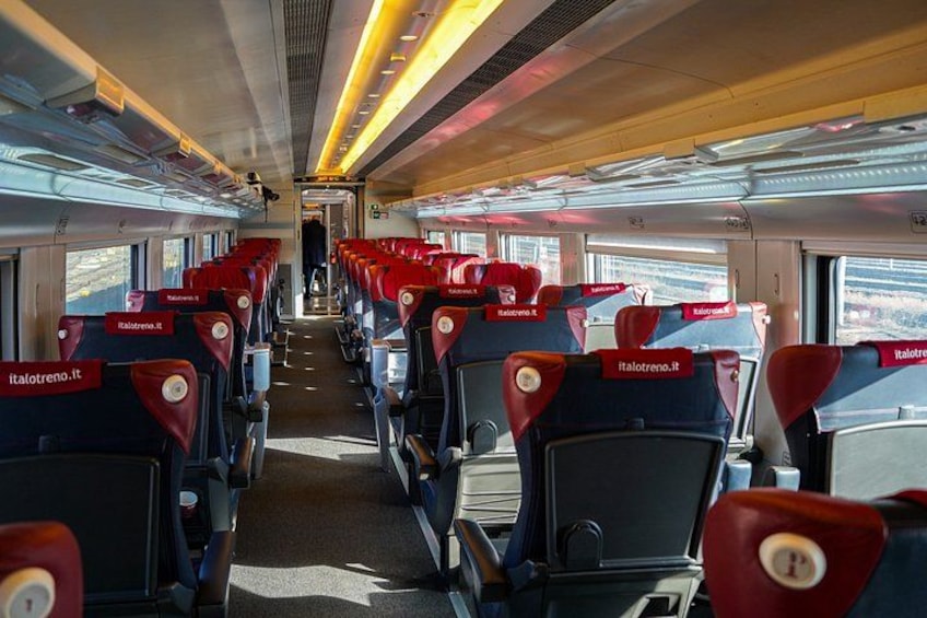 A train interior with rows of red and black seats, overhead luggage compartments, and windows. 4