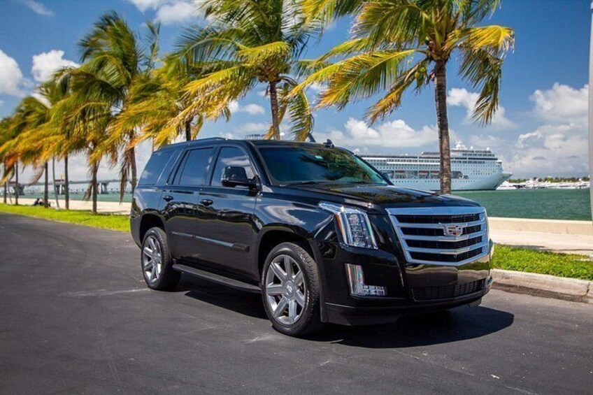 A black Cadillac SUV parked on a road with palm trees and a cruise ship in the background. 2