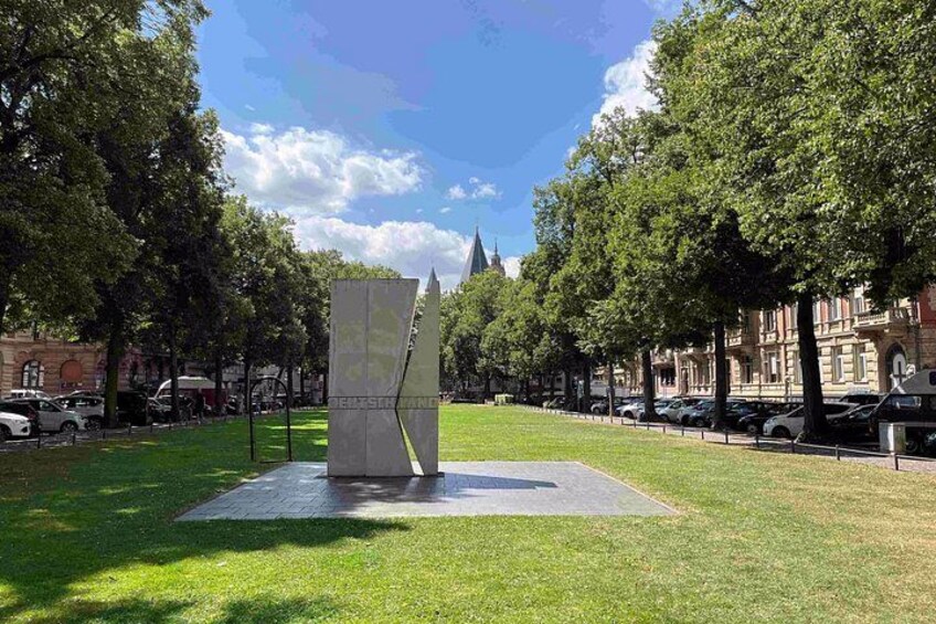 A park with a modern sculpture, green grass, trees, and parked cars. 2