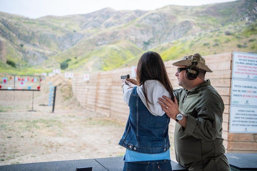 A person aiming a firearm at a target range with mountains in the background. 4