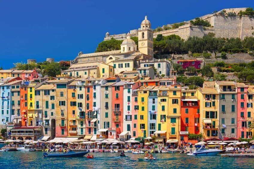 Colorful buildings along a waterfront, boats, and a historic building on a hill. 1