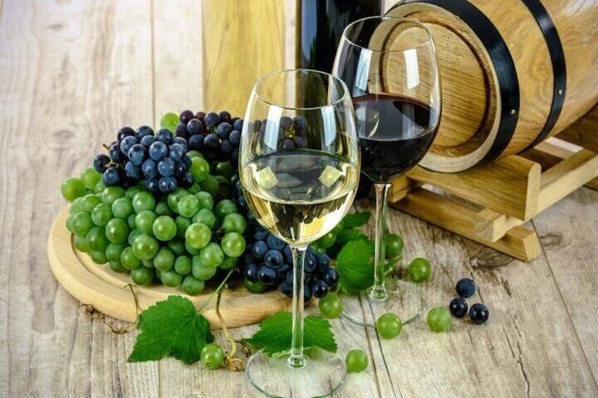 A wooden barrel, a wooden cutting board with green and black grapes, and two wine glasses filled with white and red wine. 3