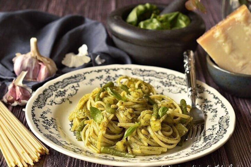 A plate of pasta with green sauce and herbs, garlic, and a bowl of spinach in the background. 5