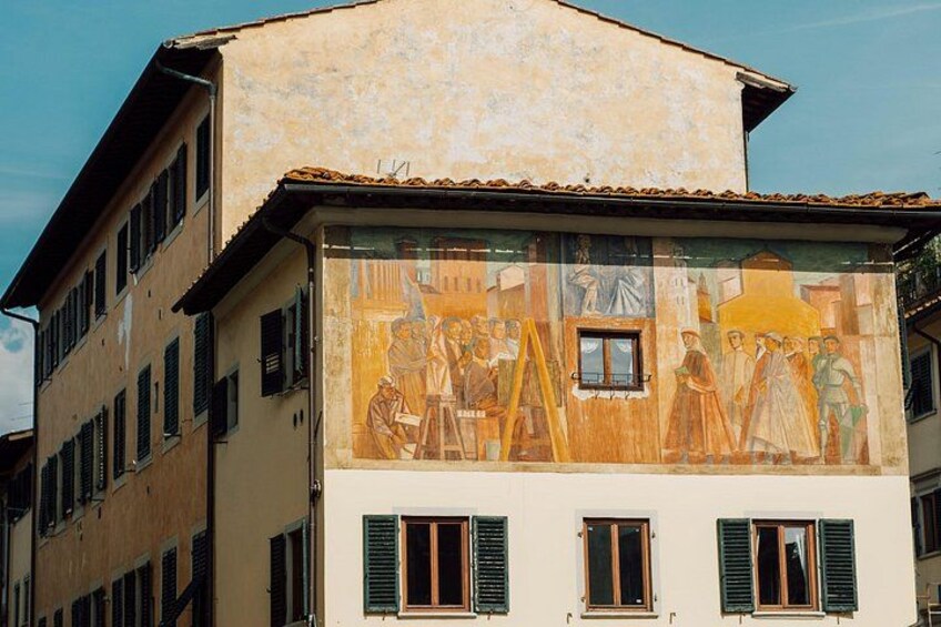 Un edificio con un affresco sulla facciata, raffigurante figure ed elementi architettonici. 2