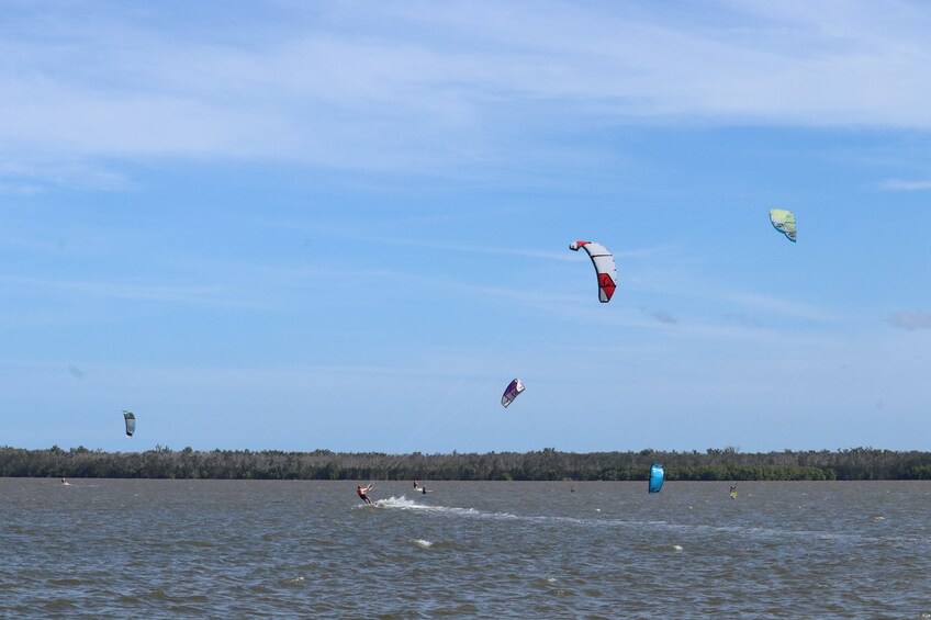Un grupo de personas practica windsurf en un lago, con varios cometas volando en el cielo. 5