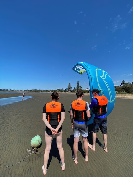 Tres personas en una playa con un paracaídas azul. 4