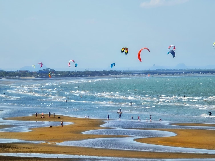 Una playa con gente y cometas coloridas volando sobre el agua. 1