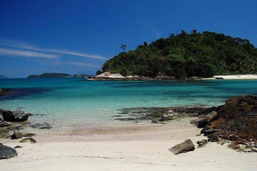 A beach with clear turquoise water, white sand, and a small island with dense greenery in the background. 3