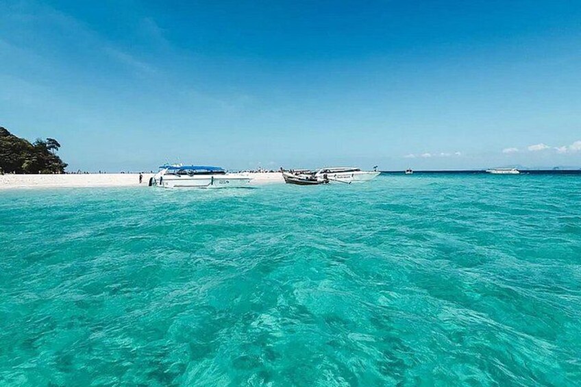 A clear turquoise sea with a boat anchored near a sandy beach. 2