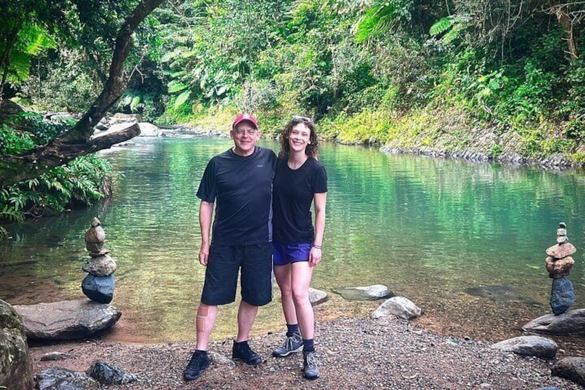 Two people standing by a river with rocks and greenery. 5