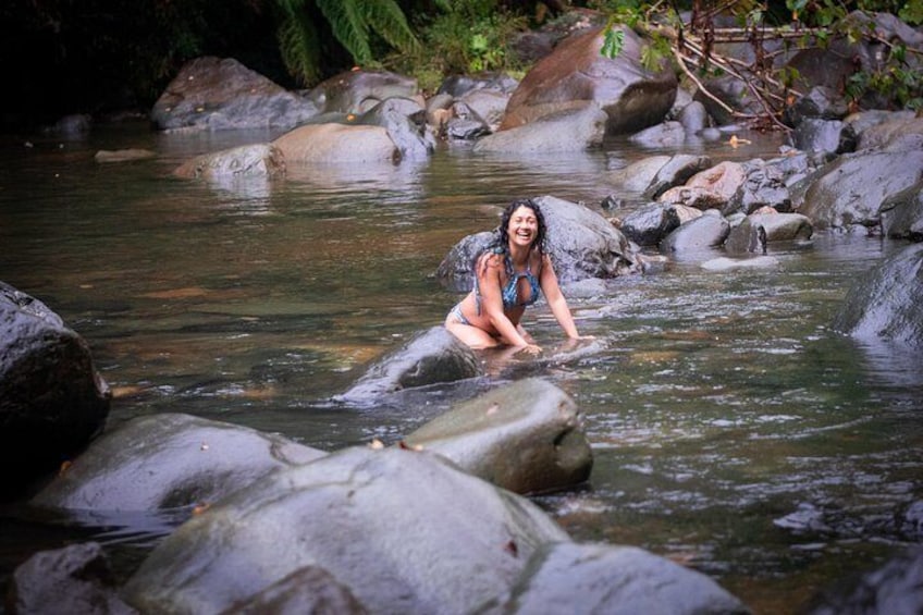 A person sitting on a rock in a river surrounded by large rocks and greenery. 4