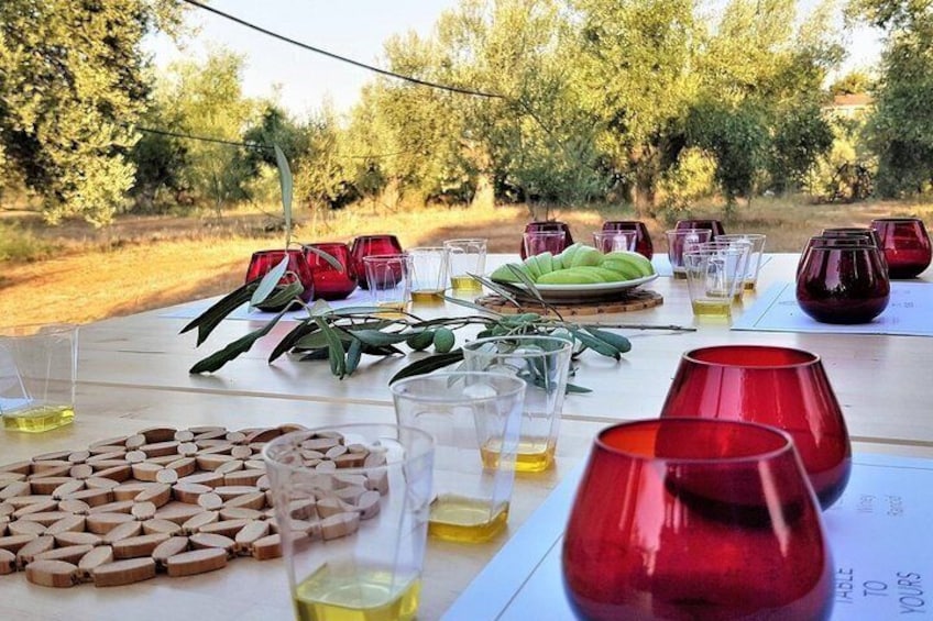 A table set outdoors with red and clear glasses, olive branches, and wooden coasters. 2