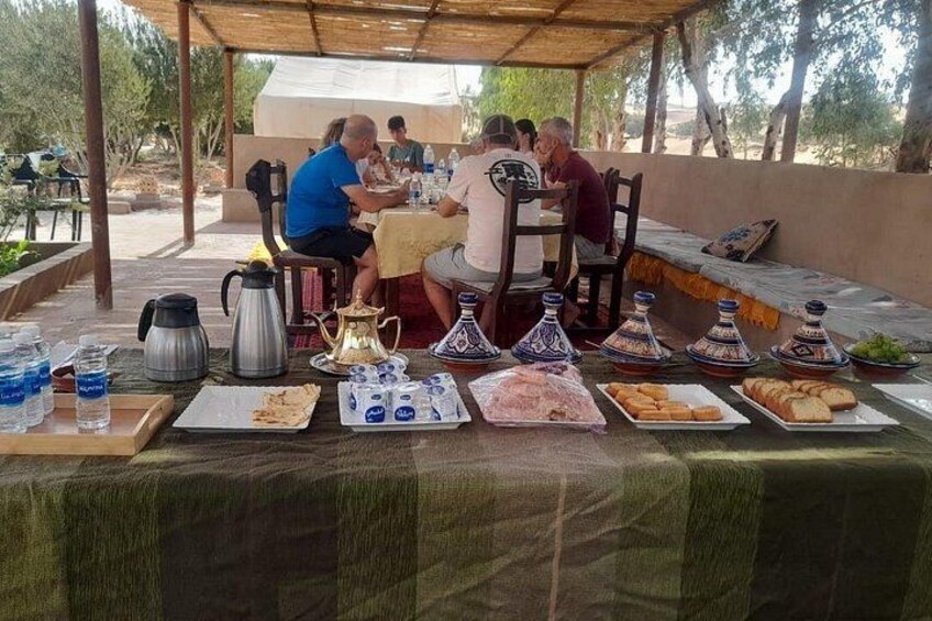 A group of people dining outdoors with a table set with various dishes and drinks. 2