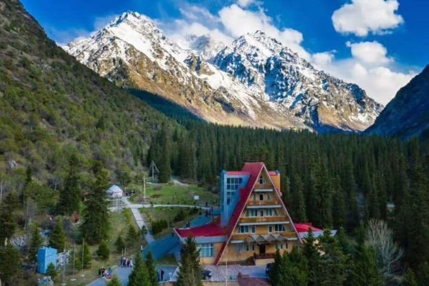 A mountain lodge with a red roof, surrounded by dense forest and snow-capped peaks. 3