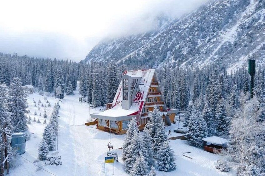 A snow-covered mountain lodge with a unique triangular roof, surrounded by snow-laden trees and a ski slope. 2
