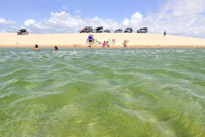 A beach with clear water, people swimming, and vehicles parked on the sand. 2