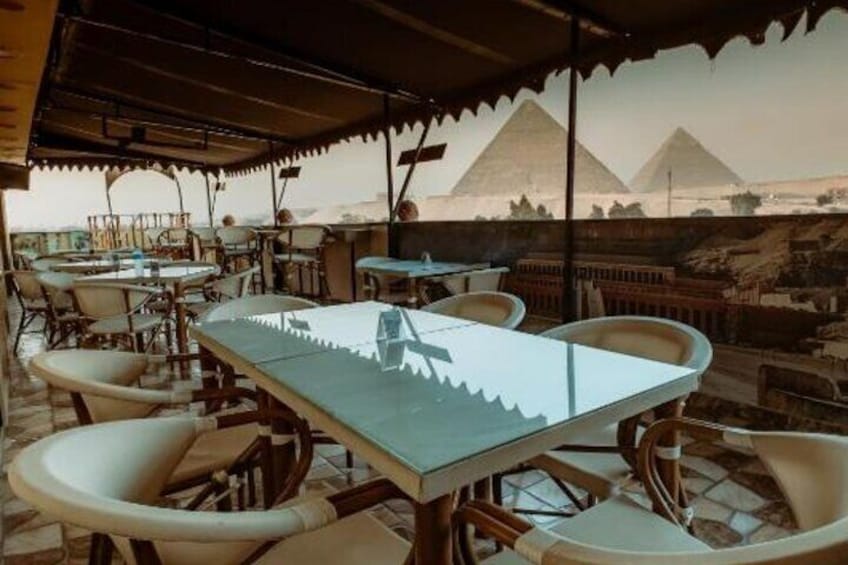 An outdoor dining area with tables and chairs, a view of the pyramids in the background. 2