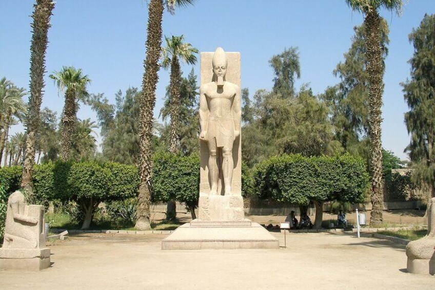 A large stone statue in a park with palm trees and bushes. 5