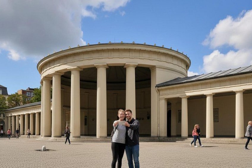 A classical building with columns, a paved courtyard, and a few people walking. 1