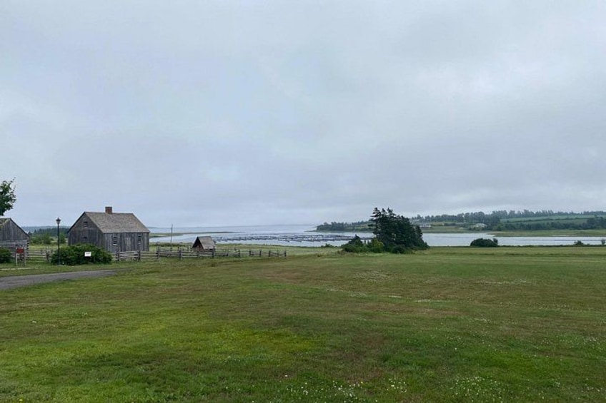 A rural landscape with a grassy field, a wooden barn, and a body of water in the distance. 2