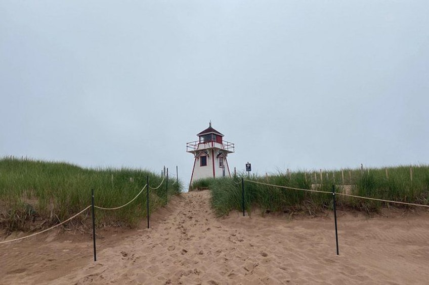 A sandy beach leading to a lighthouse with a red and white structure, surrounded by tall grass. 4