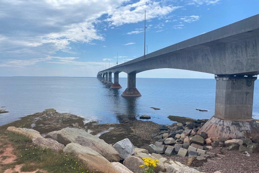 A concrete bridge over calm water, with large rocks and sparse vegetation in the foreground. 3