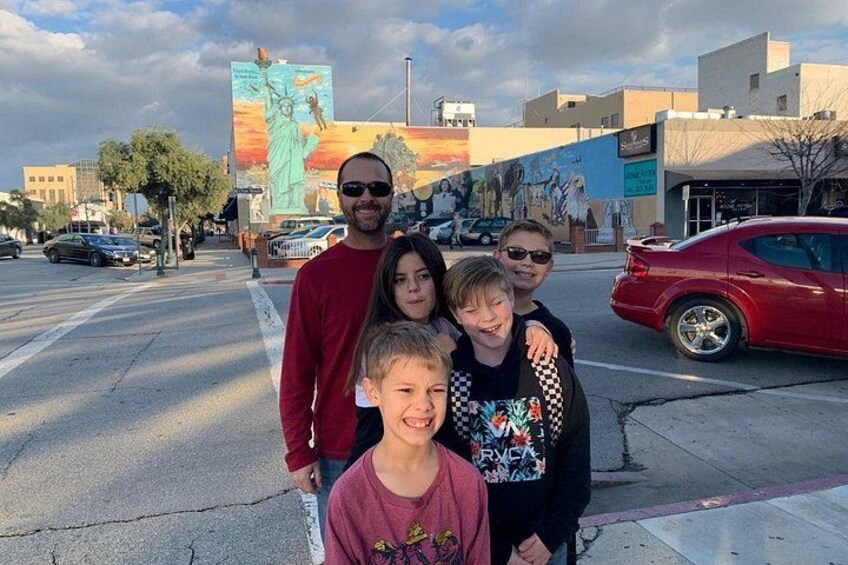 A group of people standing on a street with a mural of the Statue of Liberty in the background. 2
