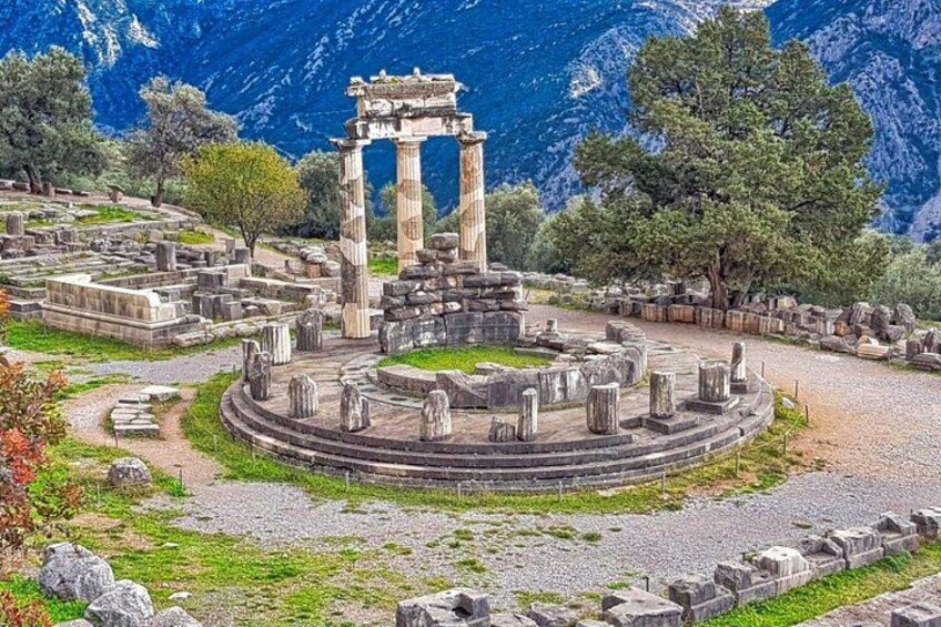Ancient ruins with columns and a circular structure, surrounded by trees and mountains. 1