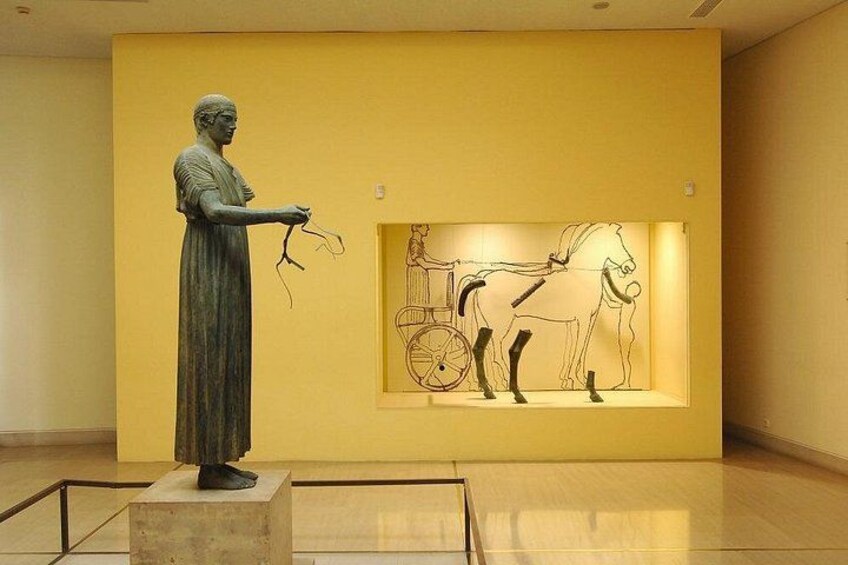 A statue of a woman holding a lyre, with a horse-drawn chariot in the background. 3