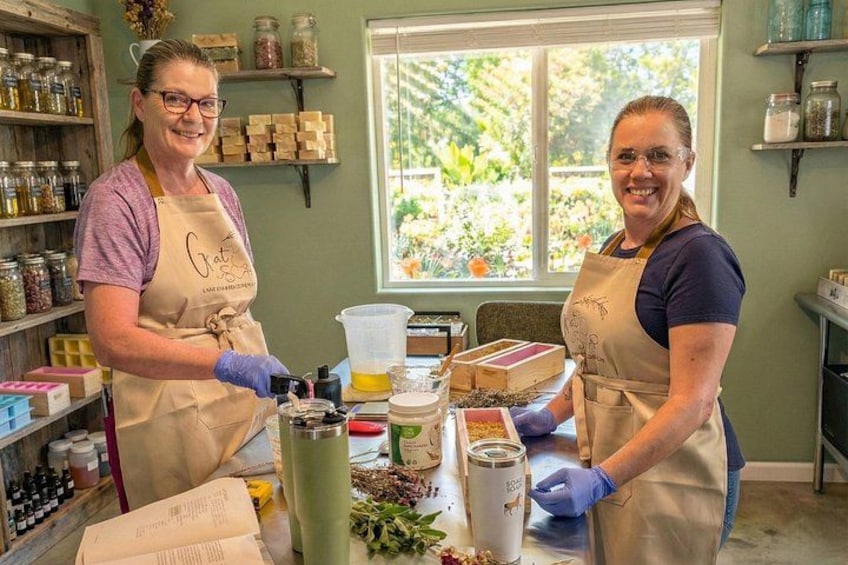 Two individuals in aprons working at a counter with jars, a scale, and various containers. 1