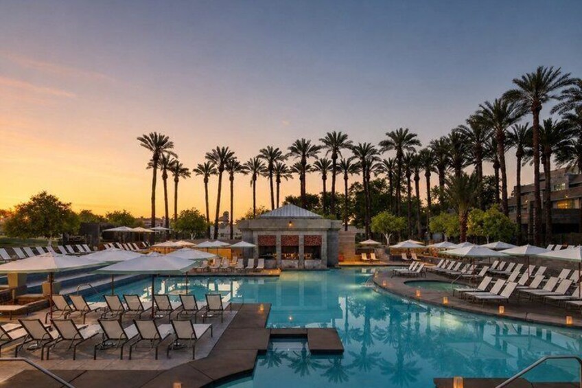 A resort pool with lounge chairs, palm trees, and a building in the background. 2