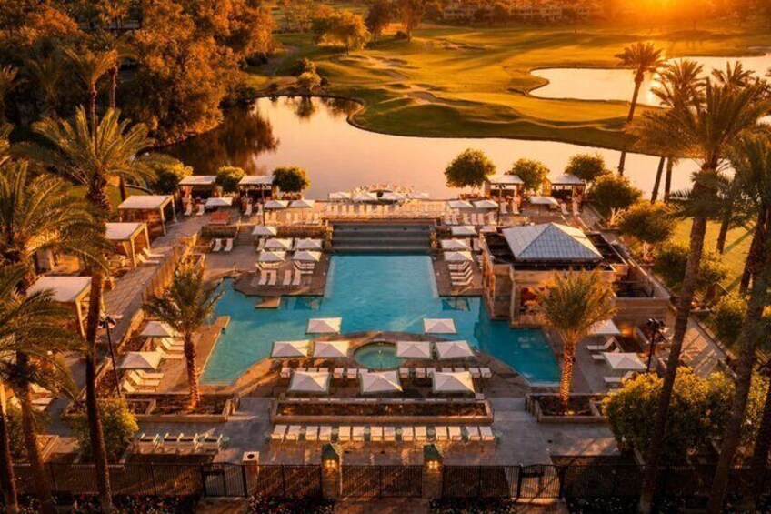 A resort pool with lounge chairs, palm trees, and a golf course in the background. 1