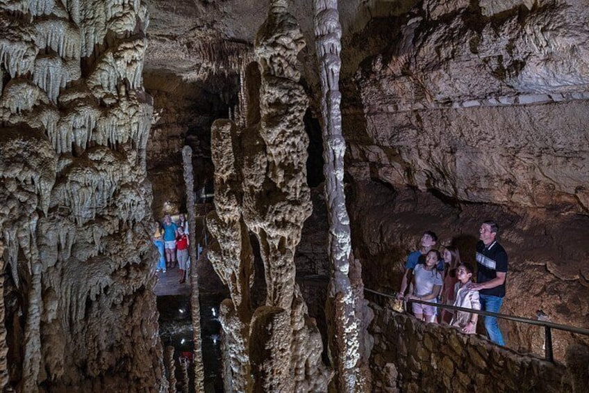 A cave with stalactites and stalagmites, a group of people observing, and a metal railing. 2