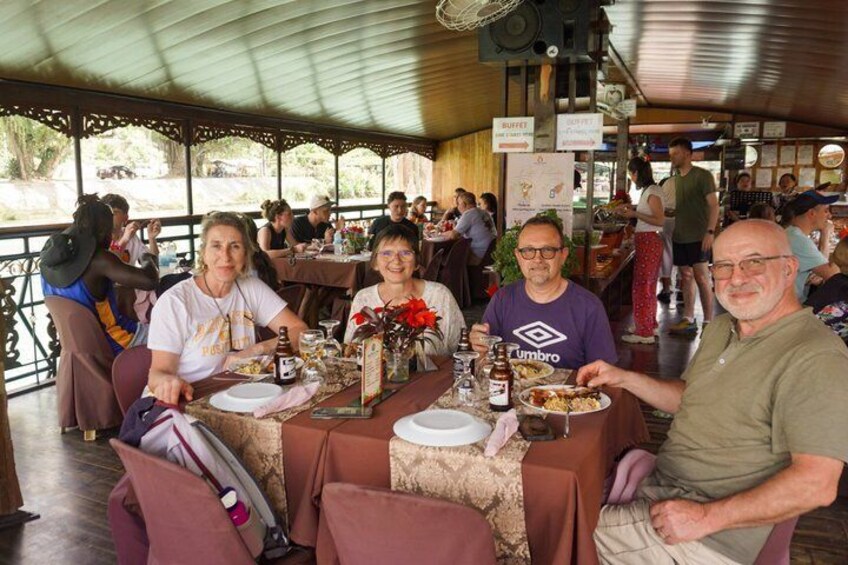 A group of people dining at an outdoor restaurant with tables covered in tablecloths and various dishes. 3