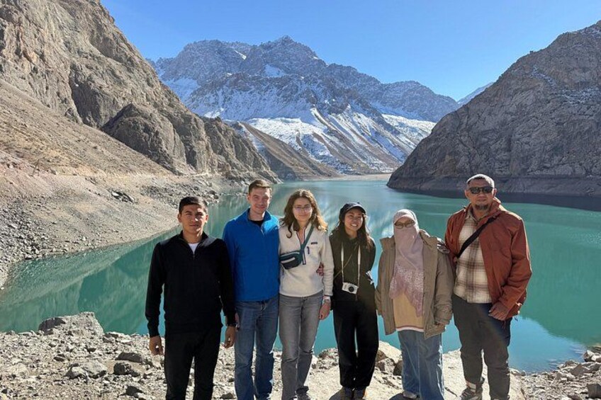 Un groupe de personnes se tient près d’un lac turquoise, avec des montagnes en arrière-plan. 5