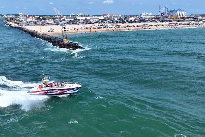 Ein Schnellboot auf dem Wasser, ein Strand und ein Steg mit Gebäuden im Hintergrund. 5