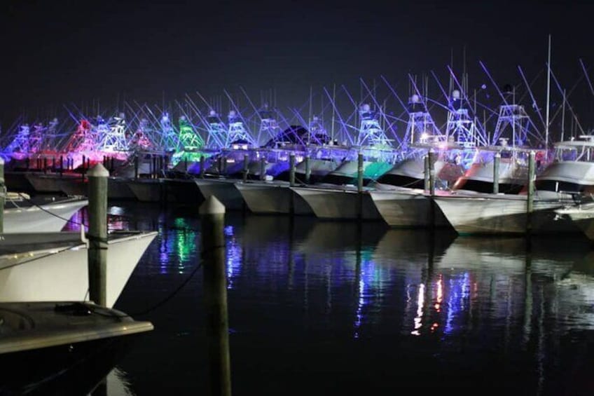 Ein Yachthafen bei Nacht mit vertäuten Booten und bunten Lichtern, die sich im Wasser spiegeln. 3