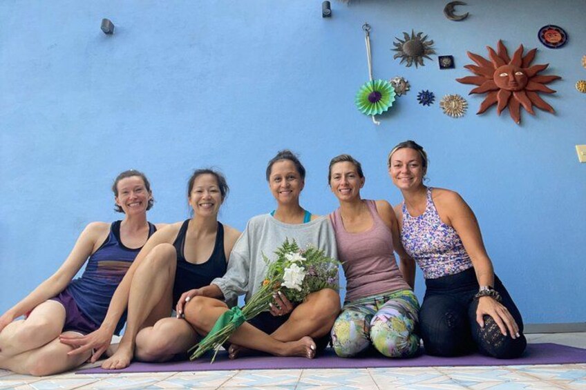 Five people sitting on a mat against a blue wall with decorative items. 2