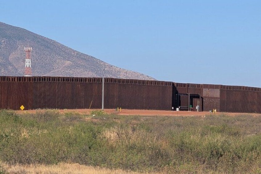 A large, long building with a flat roof, a small entrance, and a clear sky in the background. 1