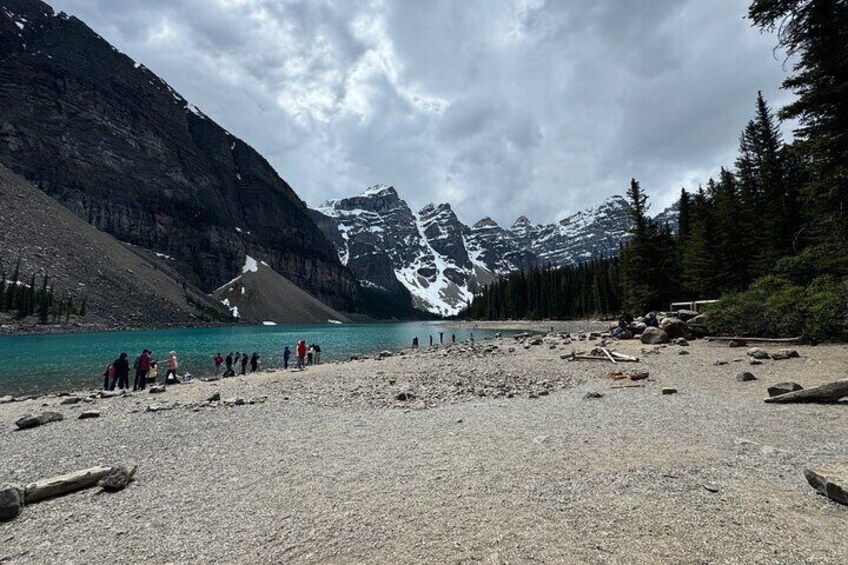 Un rivage rocheux où se trouve un groupe de personnes, un lac turquoise et, en arrière-plan, des montagnes aux sommets enneigés. 3