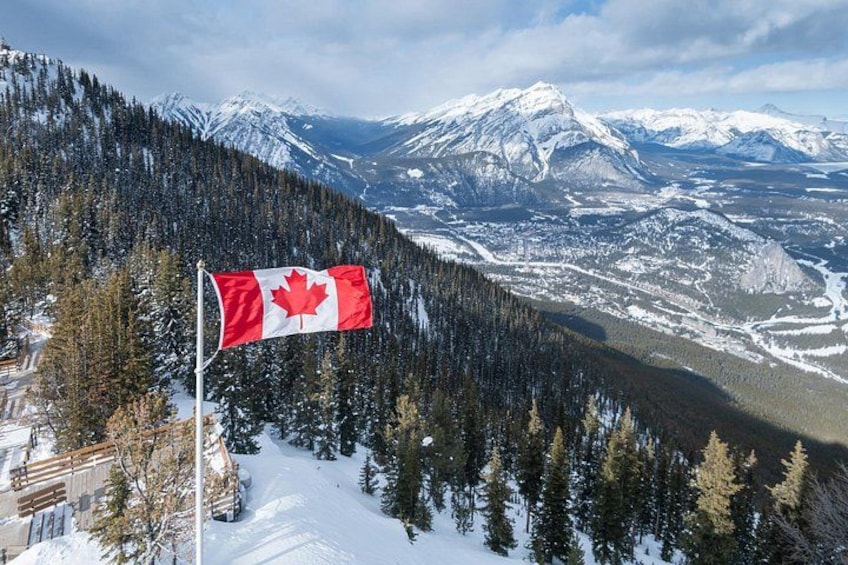 A Canadian flag on a flagpole, snow-covered mountains, and a forested valley. 3